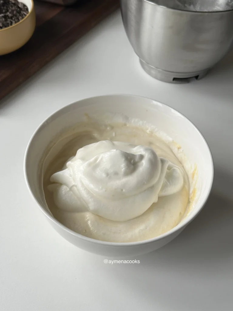 Stiff whipped egg whites added on top of the egg yolk batter, ready to be folded in.
