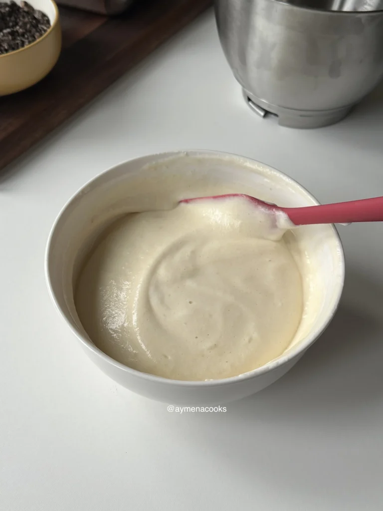 A pink silicone spatula folding the egg whites into the batter until light and airy.