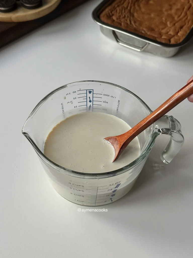 Evaporated milk, condensed milk and milk being stirred together in a glass measuring cup.