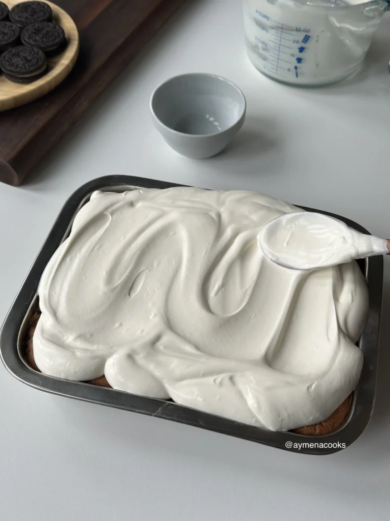 Whipped cream spread in a thick, swirled layer over the milk-soaked Oreo tres leches cake.