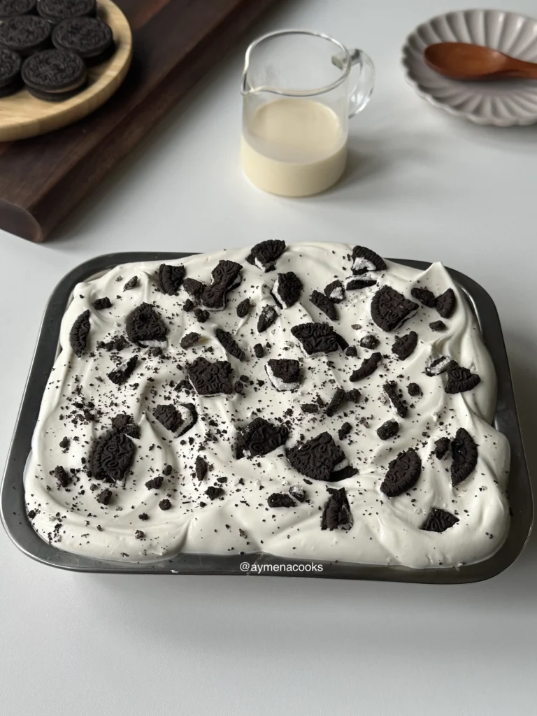 A whole Oreo tres leches cake in a baking pan, topped with a thick layer of whipped cream and crushed Oreos.