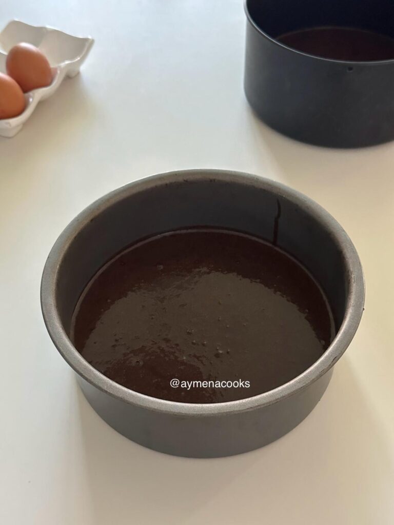 Chocolate cake batter added to a lined round cake pan.