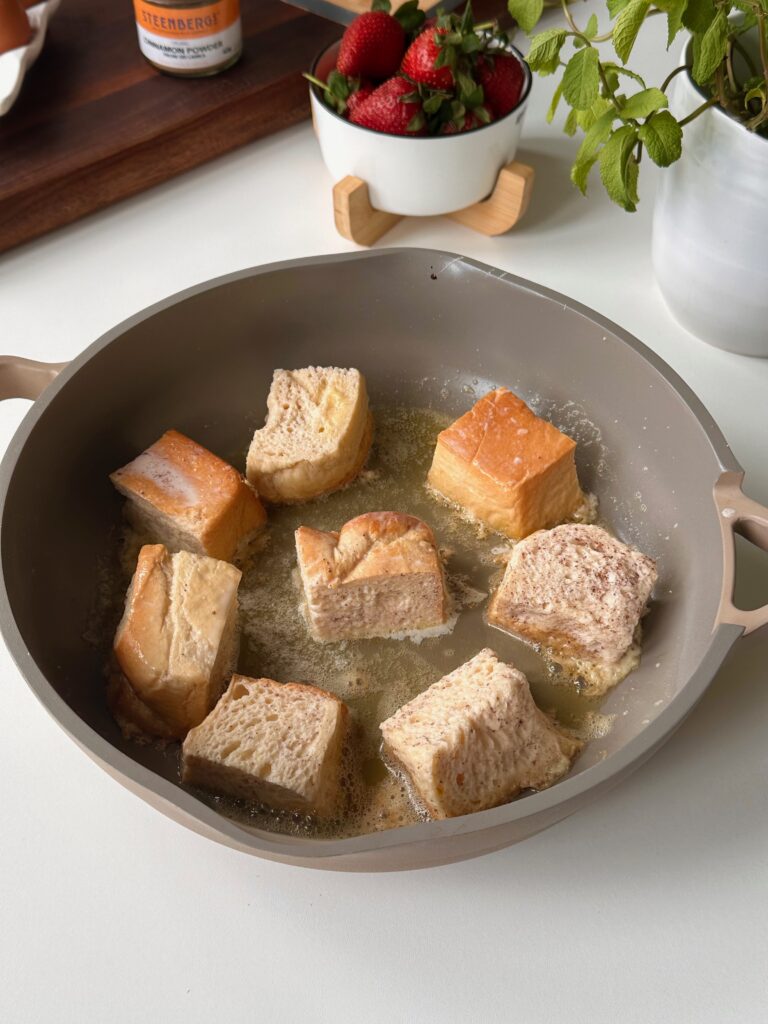 Brioche French toast bites cooking in butter in a frying pan until golden.