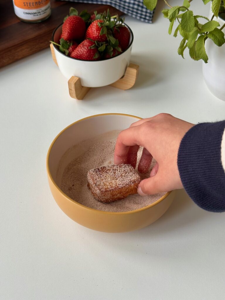 Warm brioche French toast bites being coated in cinnamon sugar.