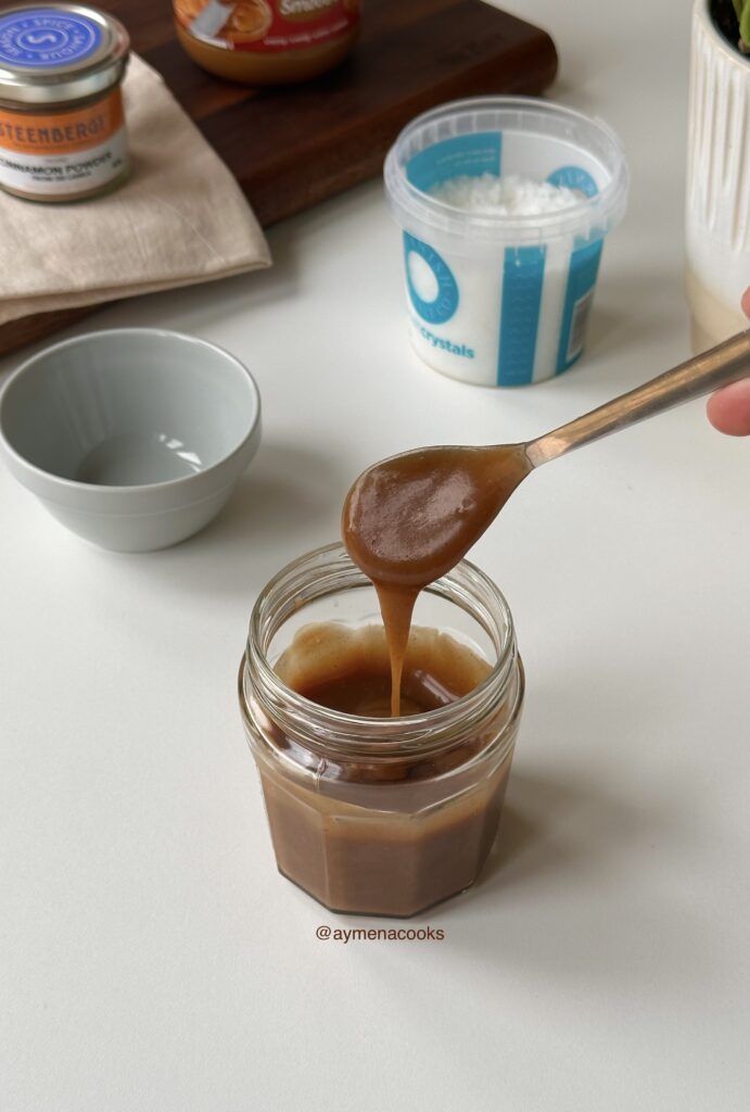 Smooth cookie butter syrup in a glass jar with a spoon showing its pourable texture.