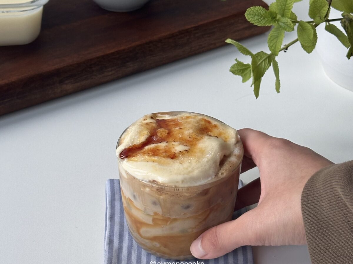 Creme brulee latte in a glass with a torched sugar top, held on a striped napkin