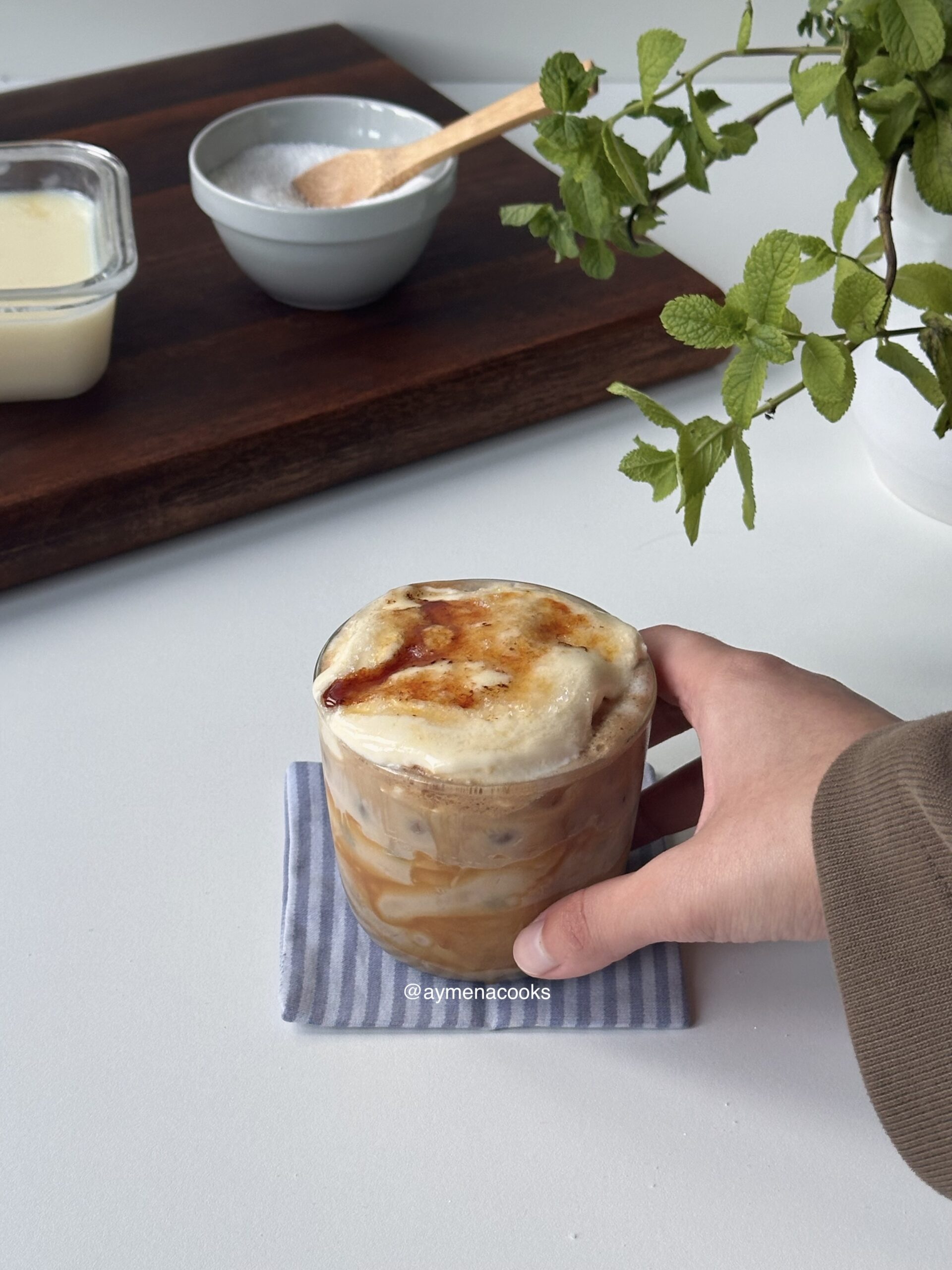 Creme brulee latte in a glass with a torched sugar top, held on a striped napkin
