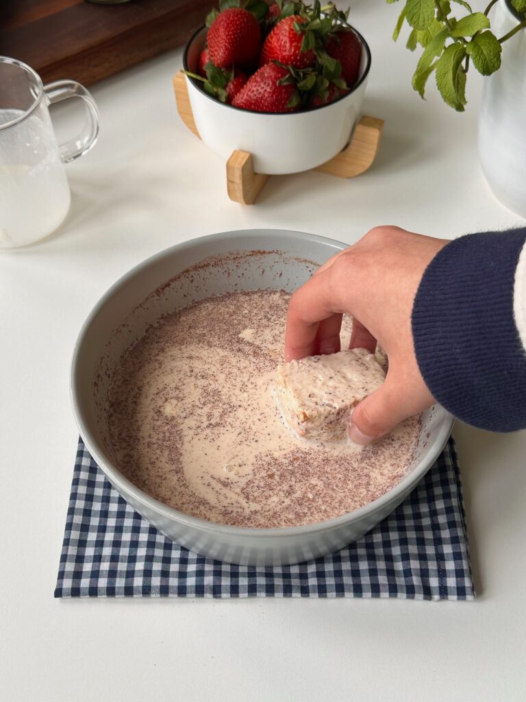Brioche pieces being dipped briefly in cinnamon and vanilla French toast custard.