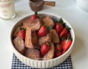 Golden cinnamon-sugar French toast bites piled in a bowl with fresh strawberries.