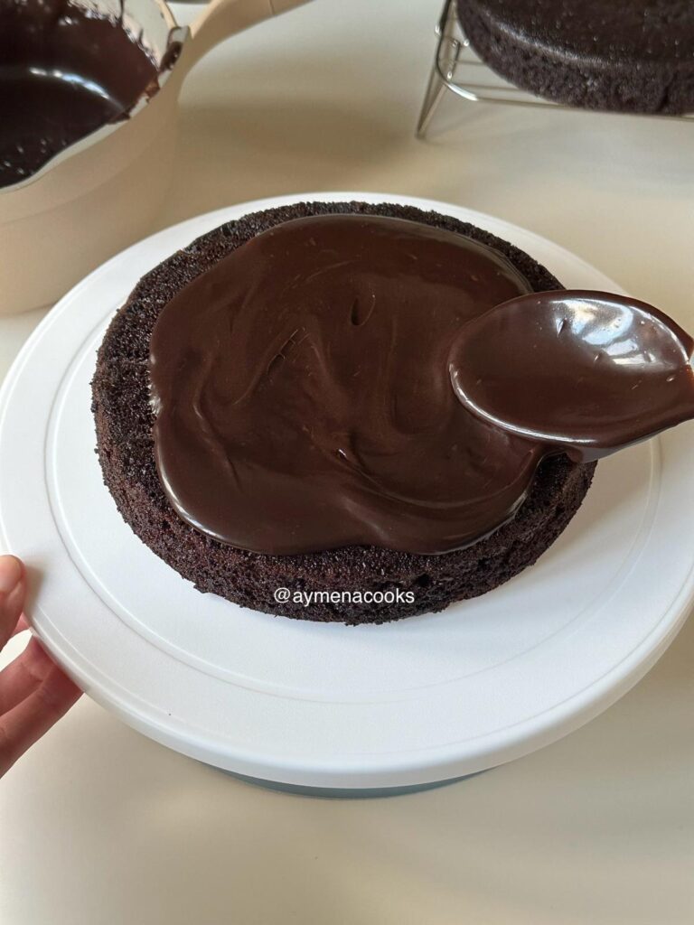 First chocolate cake layer with thick fudge frosting being spread on top