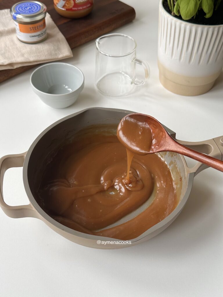 Thickened glossy cookie butter syrup coating a wooden spoon in a smooth ribbon.