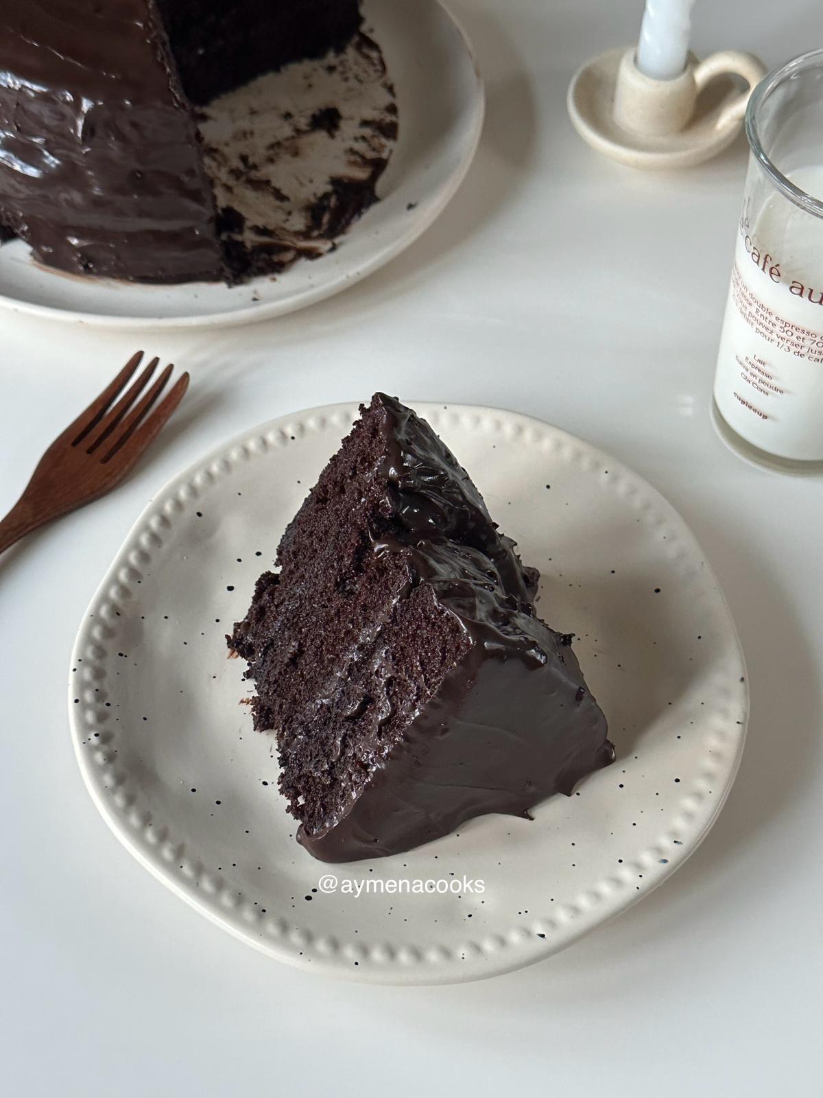 A thick slice of three-layer Matilda chocolate cake covered in glossy fudge frosting.