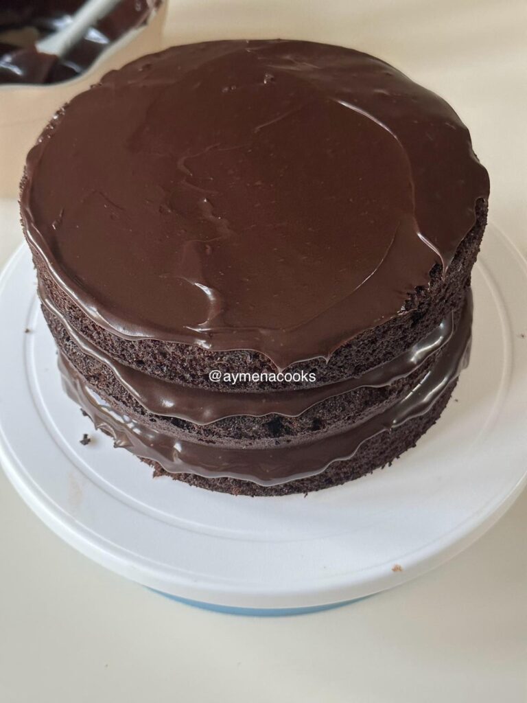 Three chocolate cake layers stacked with thick fudge frosting between each layer.