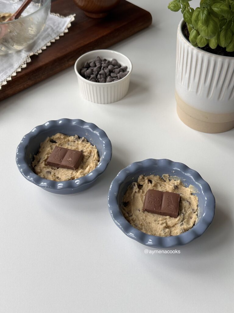 Chocolate cubes placed over a layer of cookie dough in two mini pie dishes.