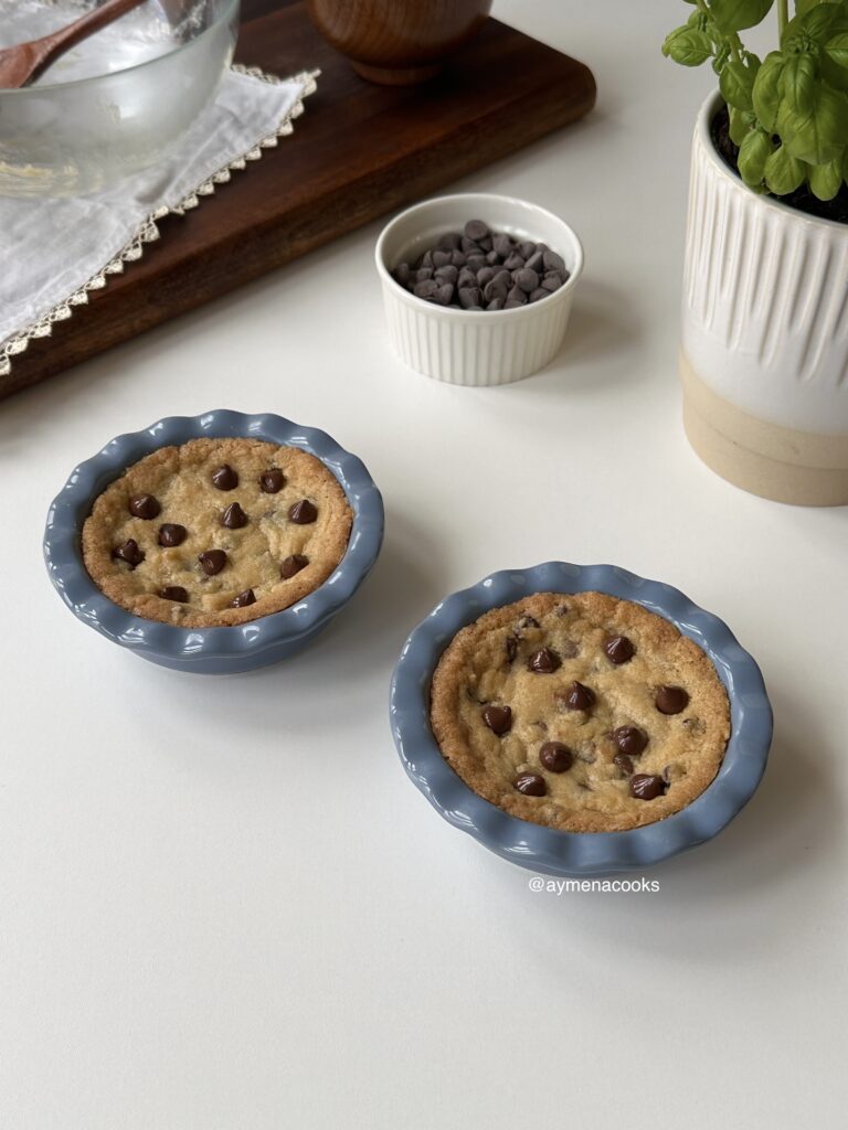 Two warm mini chocolate chip cookie pies in individual blue pie dishes.