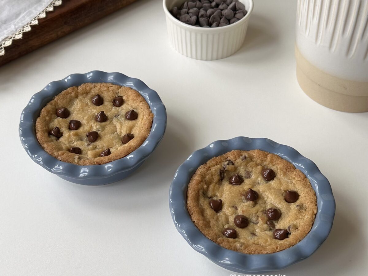 Two warm mini chocolate chip cookie pies in individual blue pie dishes.