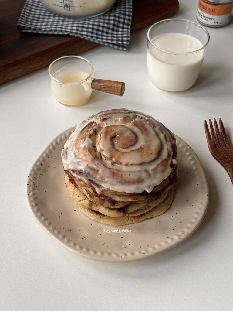 Stack of fluffy cinnamon roll pancakes with cream cheese frosting.