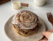 Stack of fluffy cinnamon roll pancakes with caramelized cinnamon swirls and cream cheese frosting.