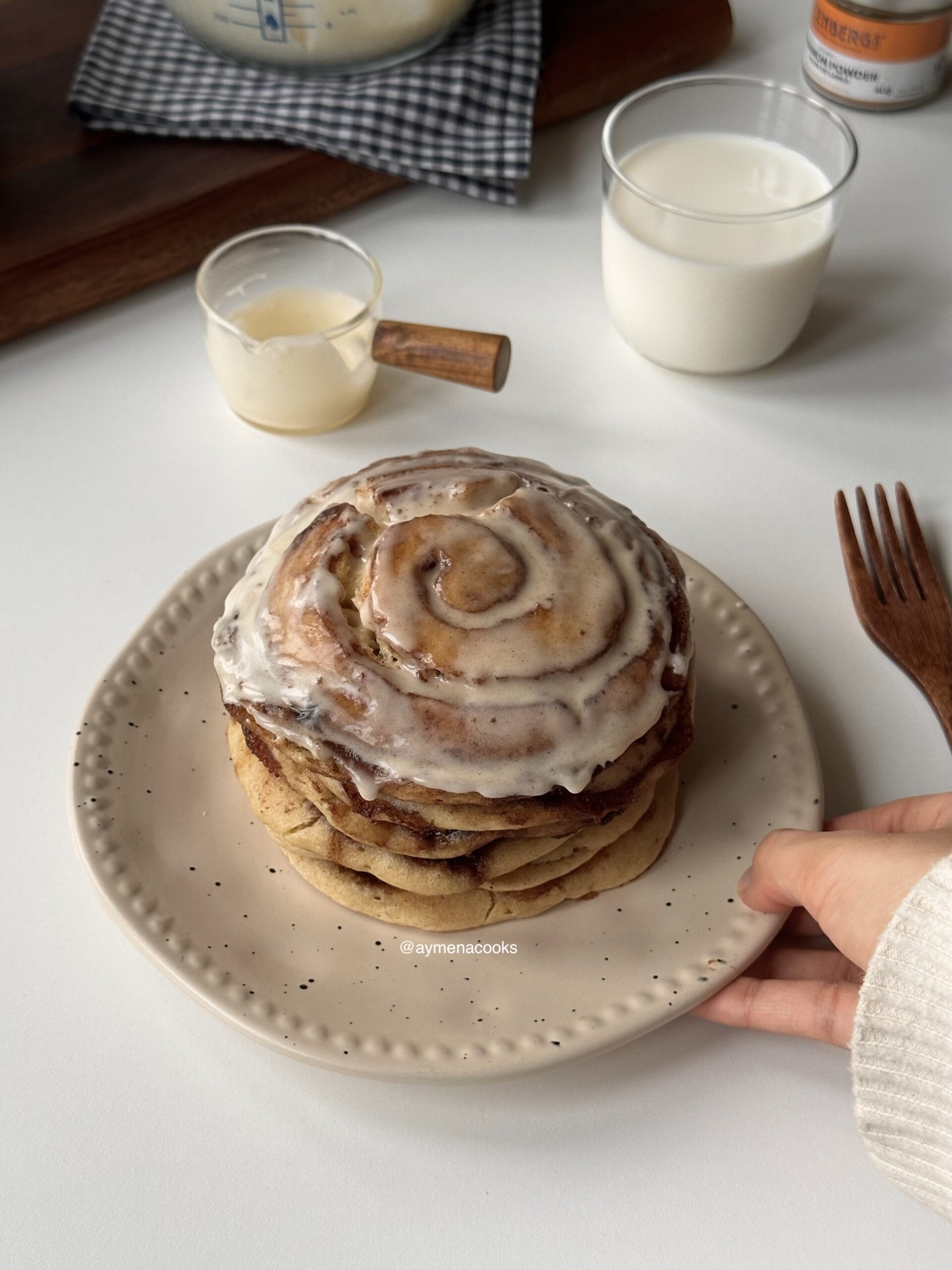 Stack of fluffy cinnamon roll pancakes with caramelized cinnamon swirls and cream cheese frosting.