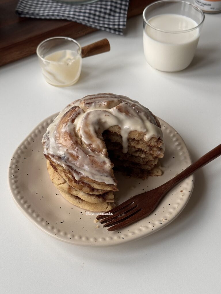 Cut cinnamon roll pancake stack showing a fluffy center, brown sugar cinnamon swirl and cream cheese frosting.