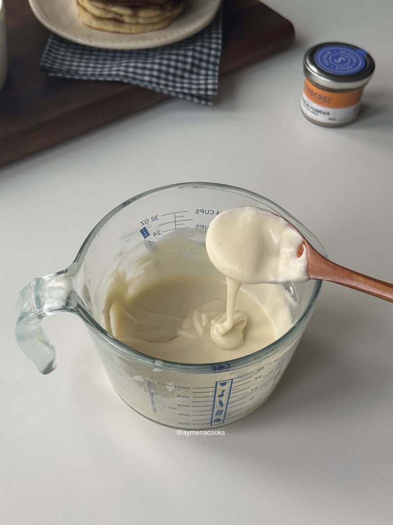 Cream cheese frosting falling from a spoon to show its thick but pourable texture.