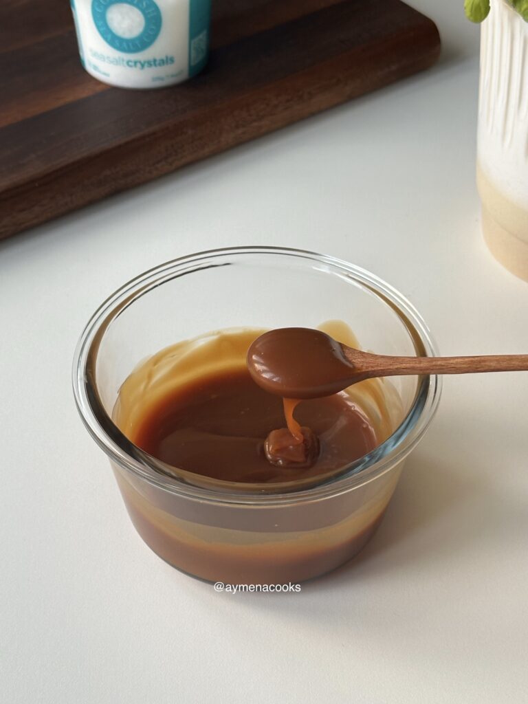 Cooled caramel sauce falling from a spoon in a thick pourable ribbon.