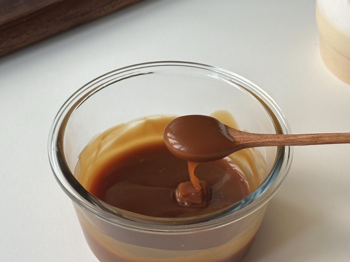 Glossy homemade caramel sauce in a glass container with a spoon showing its thick pourable texture.