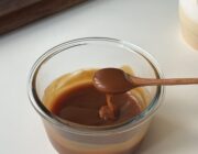 Glossy homemade caramel sauce in a glass container with a spoon showing its thick pourable texture.