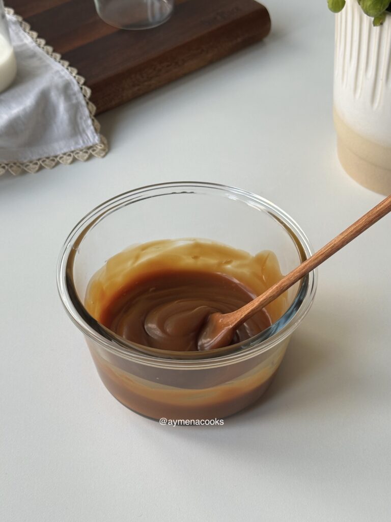 Homemade caramel sauce in a glass container with a spoon.