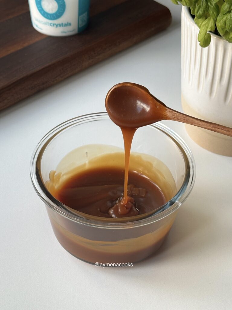 Caramel sauce falling from a spoon in a thick pourable ribbon.