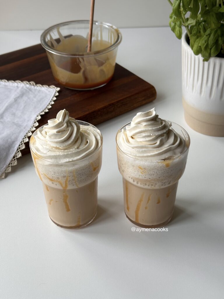 Two homemade caramel frappes topped with piped vanilla whipped cream.