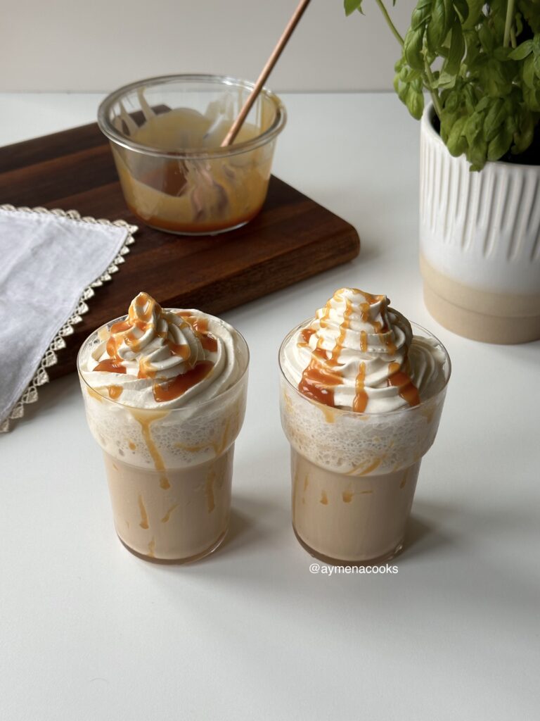 Two thick caramel coffee frappes in tall glasses with whipped cream and caramel drizzle.