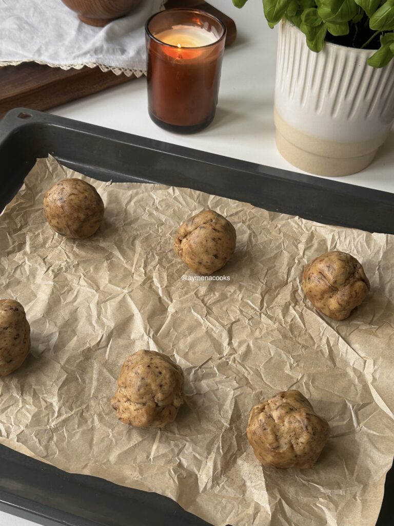 Six large portions of espresso cookie dough on a lined baking sheet.