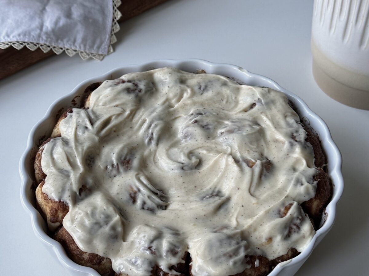 Warm cinnamon roll bites in a baking dish topped with brown butter cream cheese frosting.