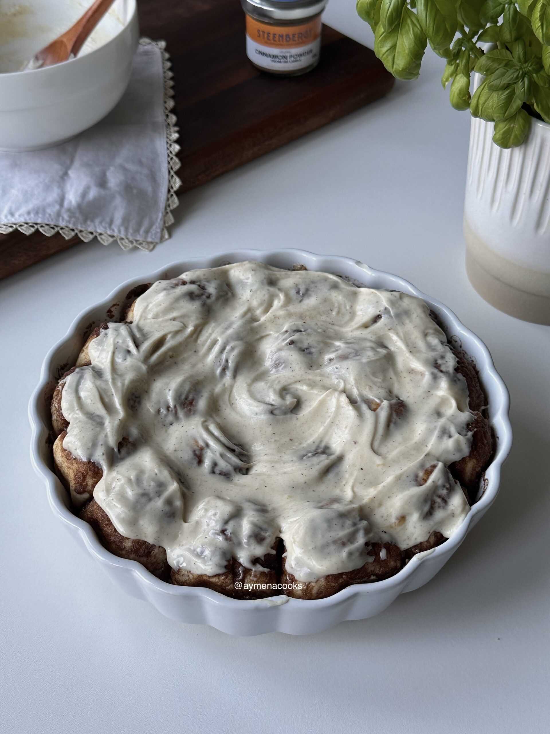 Warm cinnamon roll bites in a baking dish topped with brown butter cream cheese frosting.