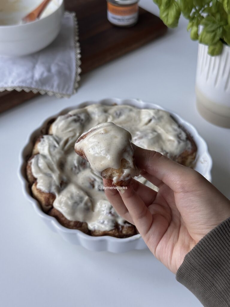One soft cinnamon roll bite lifted from the dish and topped with cream cheese frosting.