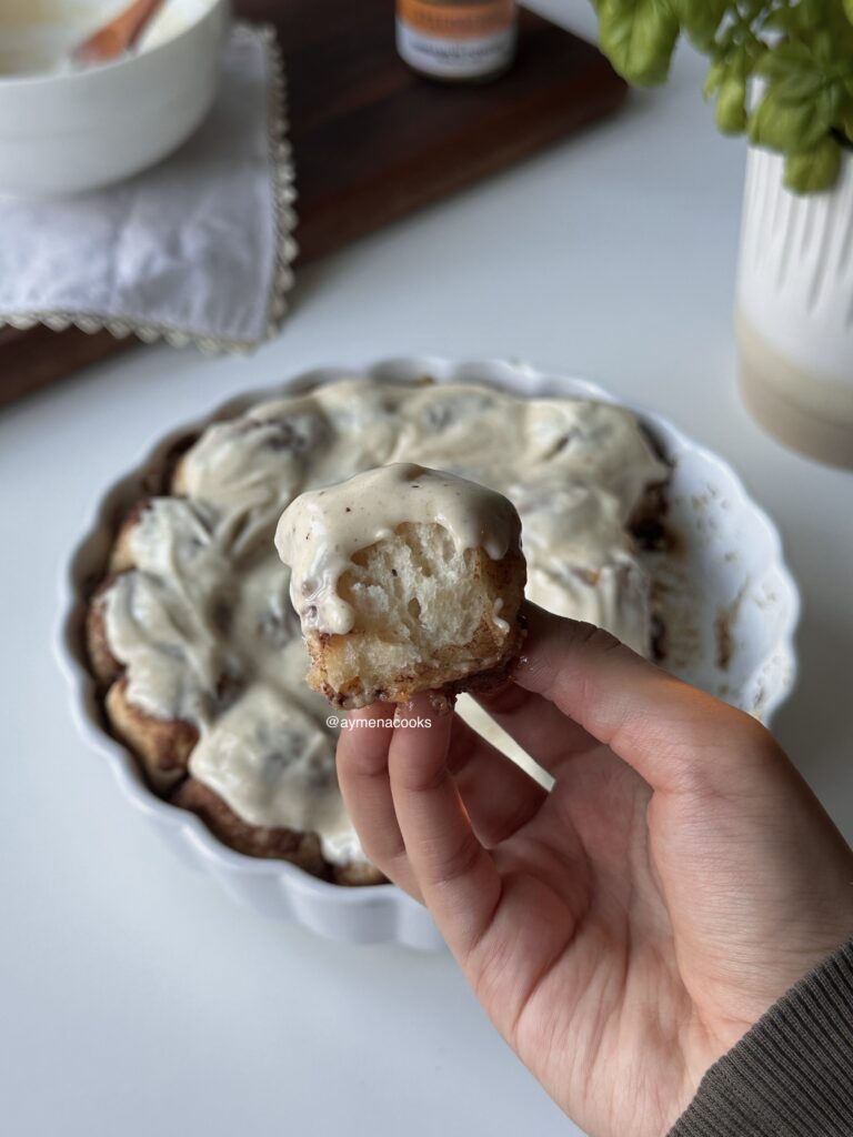 Soft frosted cinnamon roll bite pulled apart from the baking dish to show its fluffy texture.