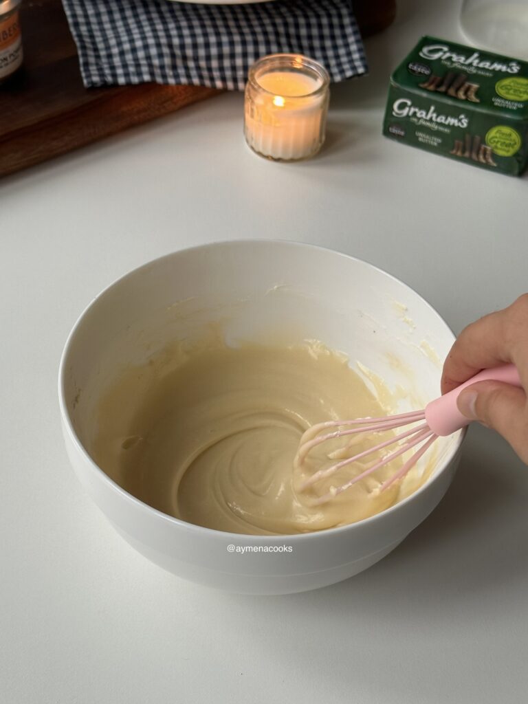 Smooth cream cheese frosting being whisked in a mixing bowl.