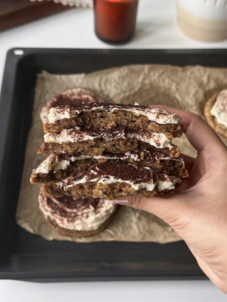 Broken tiramisu cookie halves stacked on top of each other to show the espresso cookie crumb and mascarpone frosting.